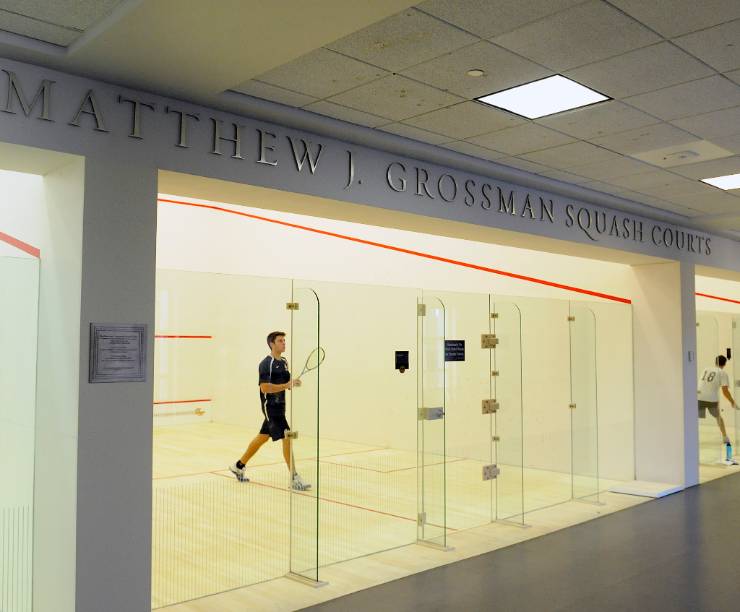Squash players take advantage of the wood-floored squash courts.  The courts are glass backed and have a sign on top that reads the Matthew J. Grossman Squash Courts.