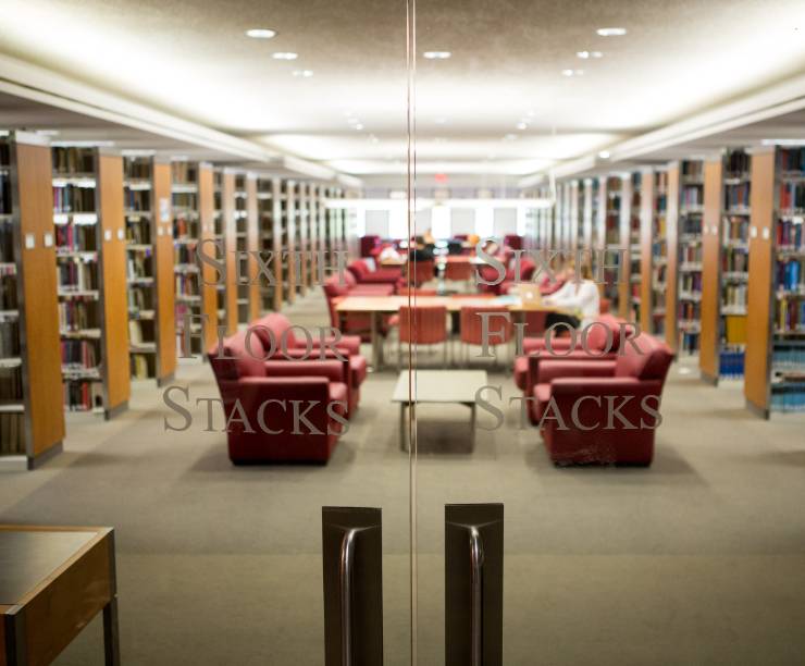 Library bookshelves and lounge chairs as seen through a glass door.