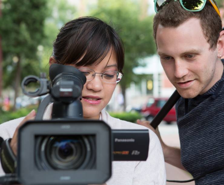 A woman holds a camera and a man stands behind her