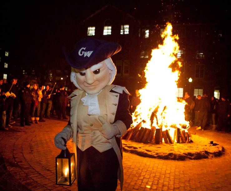 Mascot George stands in front of a bonfire at night.