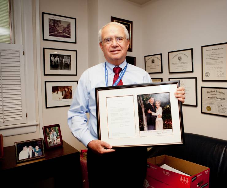 Doctor stands in his office holding a framed letter and photo of President and Mrs. Reagan.