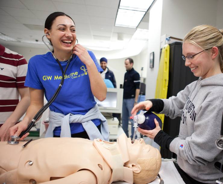 Female medical students work with simulation lab dummy. One student listens to pulse pulse and the other gives oxygen.