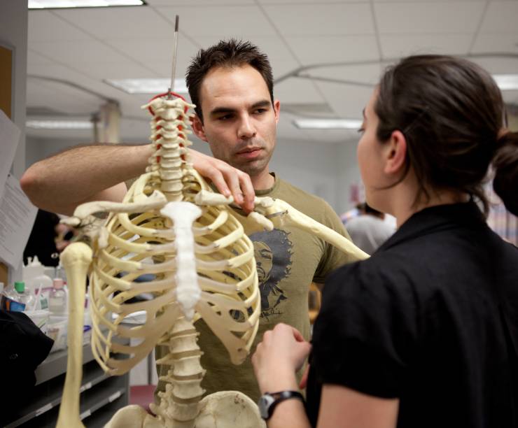 One male and one female physical therapy students examine the arm bones of a skeleton.