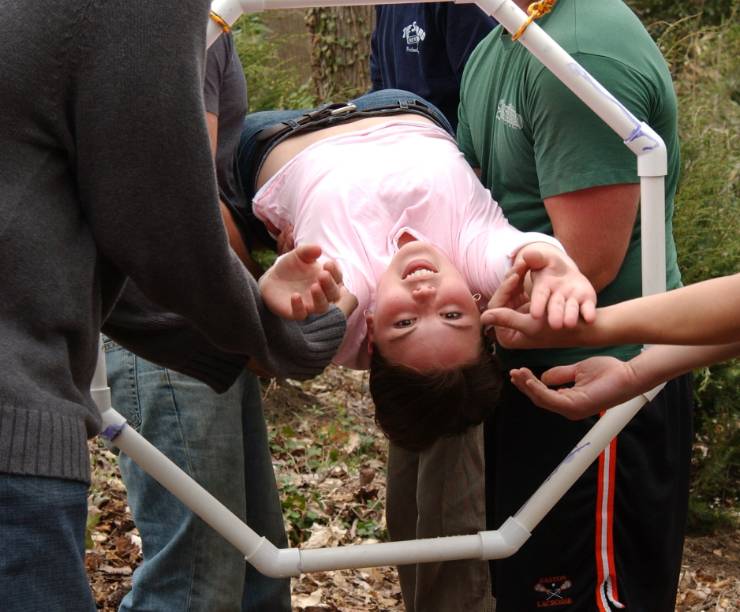 Four students hold a fifth student horizontally as they pull her through a hanging web ring.