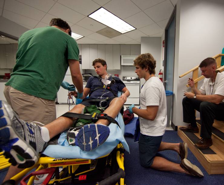 High school students learn to put a patient on a gurney while the instructor looks on