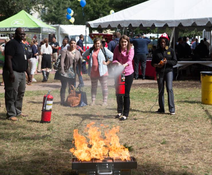 A woman uses a fire extinguisher to put out a small demonstration fire as others look on.