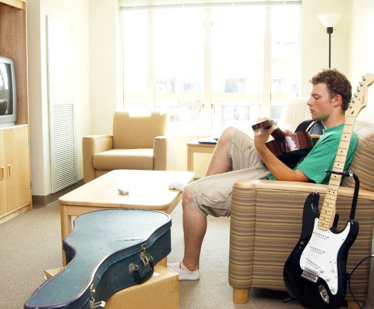 A student plays guitar on the sofa in his dorm room.