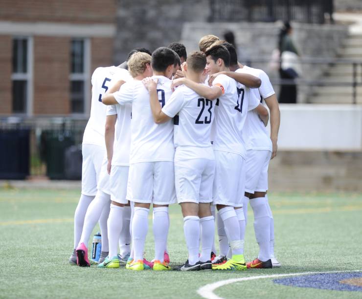 The Men's Soccer team join hands at the center of a huddle