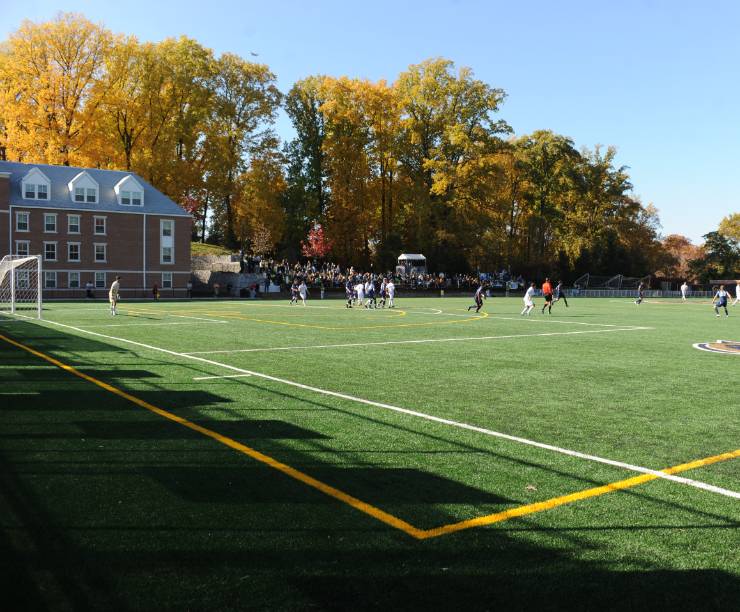 Athletic field with soccer game in progress. Brick building in left corner of the field.