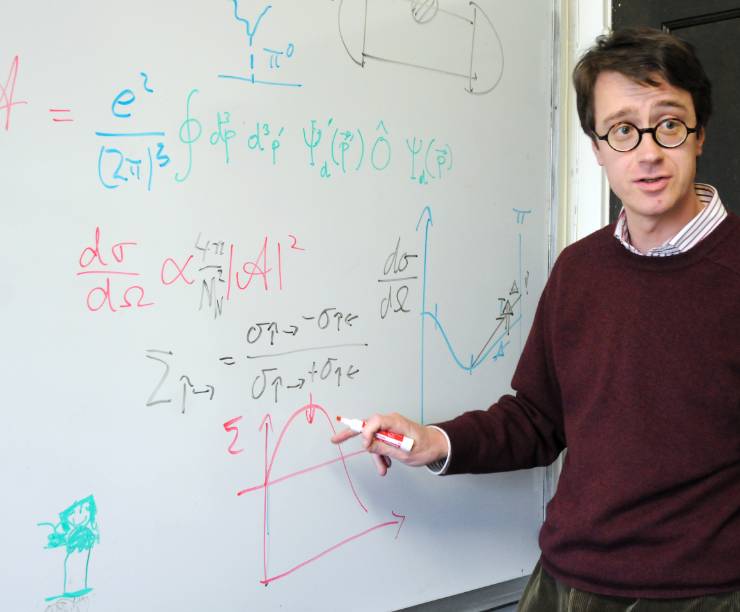 A professor stands in front of a board full of equations.