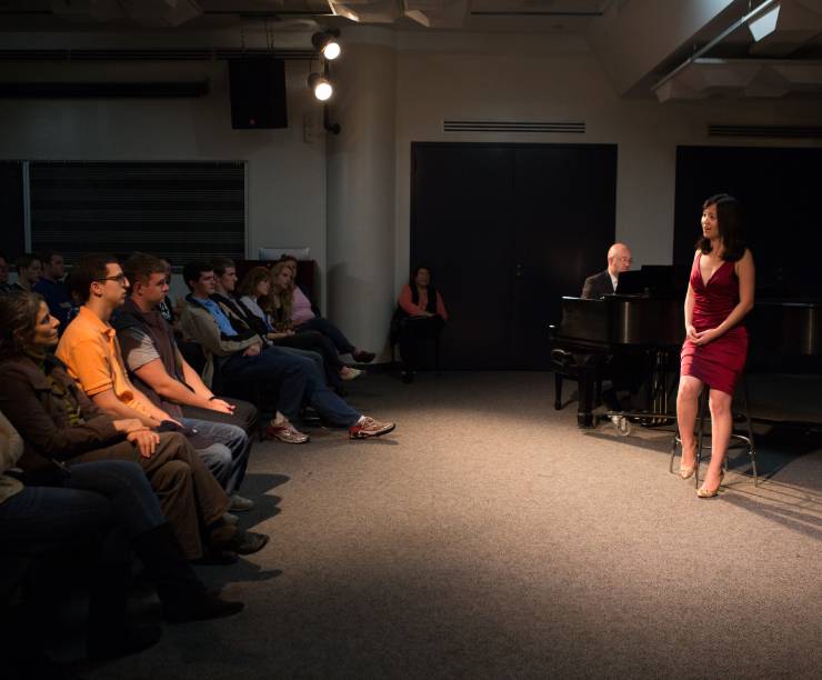 A woman sings to a piano in front of an audience.
