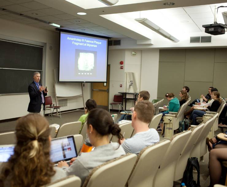 A professor lectures and shows a presentation to students in a lecture hall.