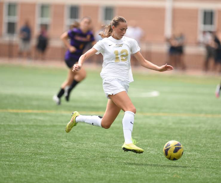 Member of the women's soccer team running down the field with the ball.
