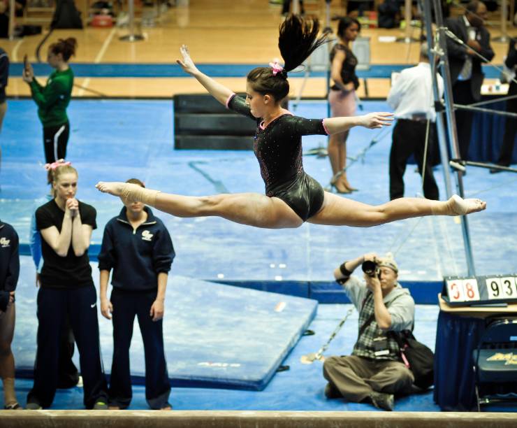 A gymnast leaps while teammates look on.