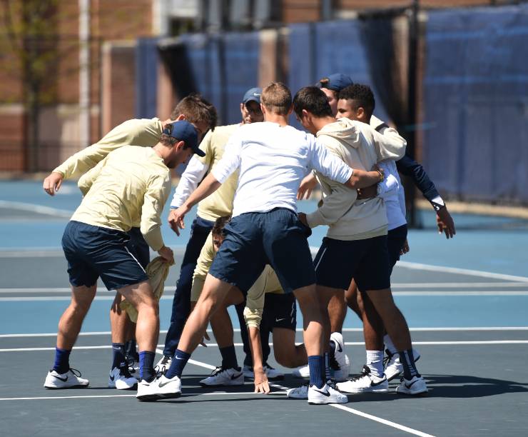 Tennis players huddle on the court.