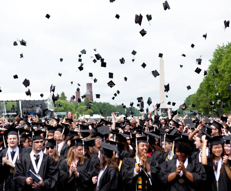 Graduates in academic regalia throw their caps in the air, with the Washington Monument in the background.