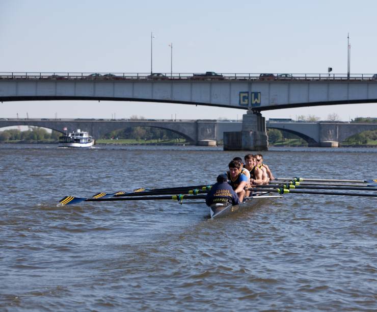 Students row on the Potomac with a bridge in the background.