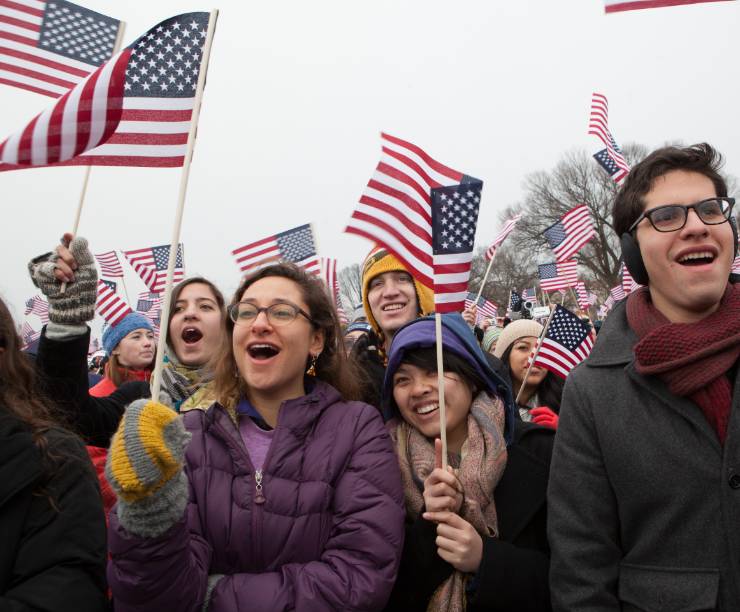 Students in a crowd wave American flags.