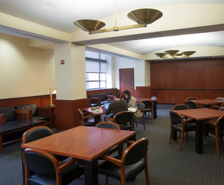GW Law's Student Conference Center with two students studying with laptops at a table with chairs. There are a number of empty tables and chairs as well.