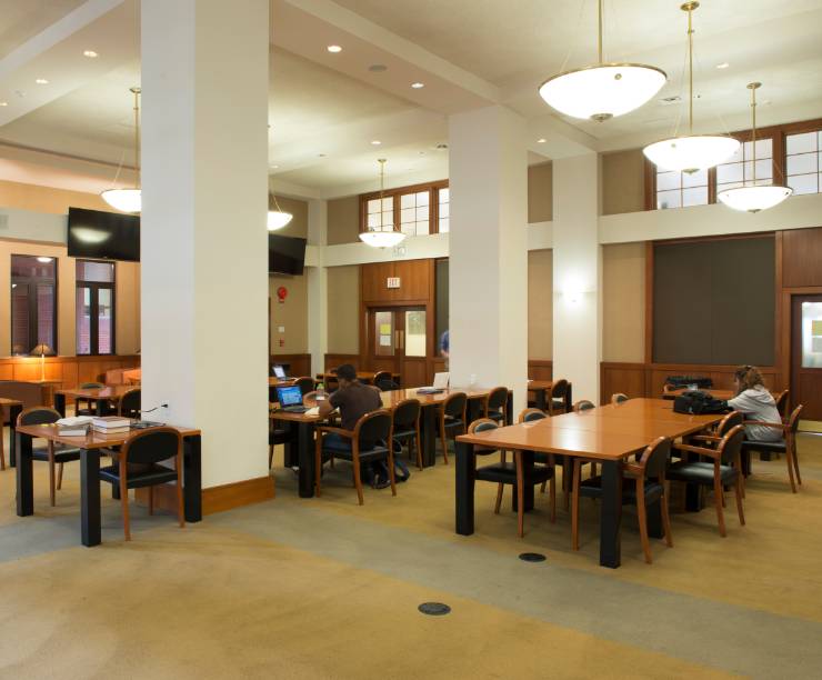 Students seated at tables in GW Law's Tasher Great Room studying with books and laptops.