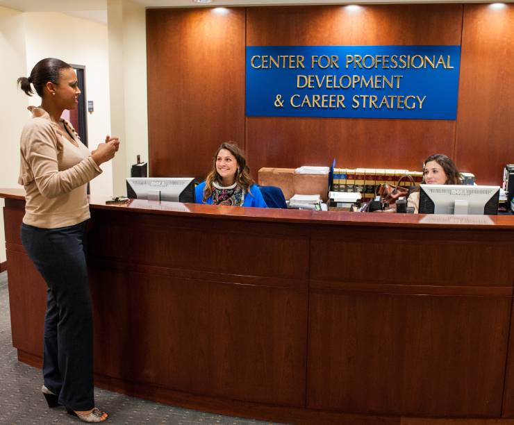 Entrance to the Career Development Office with a woman speaking to two female staff members behind a desk. A sign behind the desk reads 