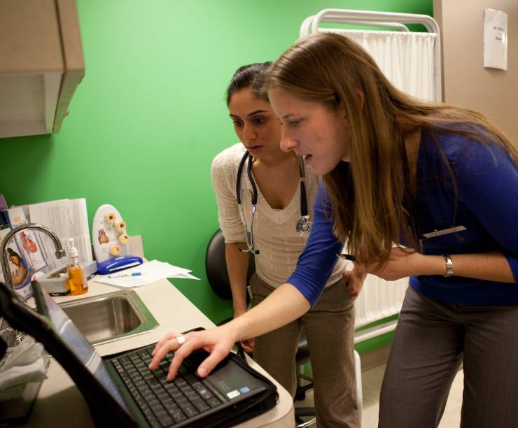Two women look at a computer in an exam room.