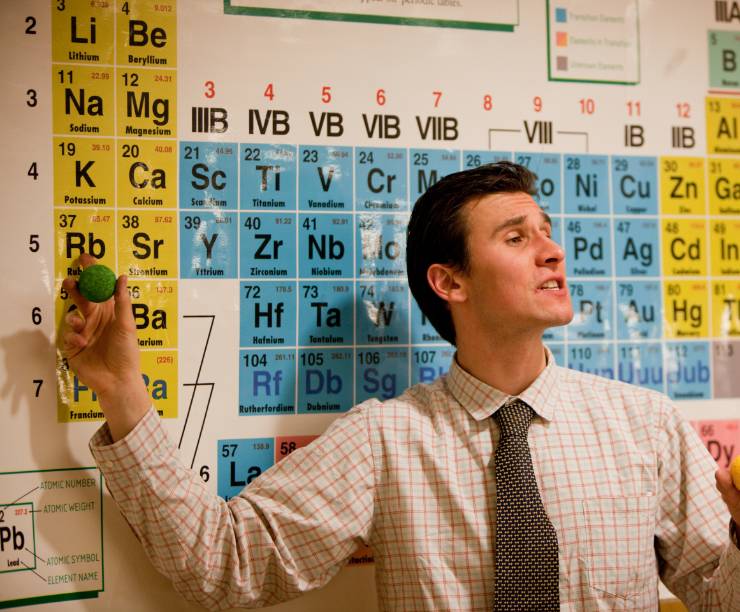 A teacher stands before the Periodic Table of Elements.