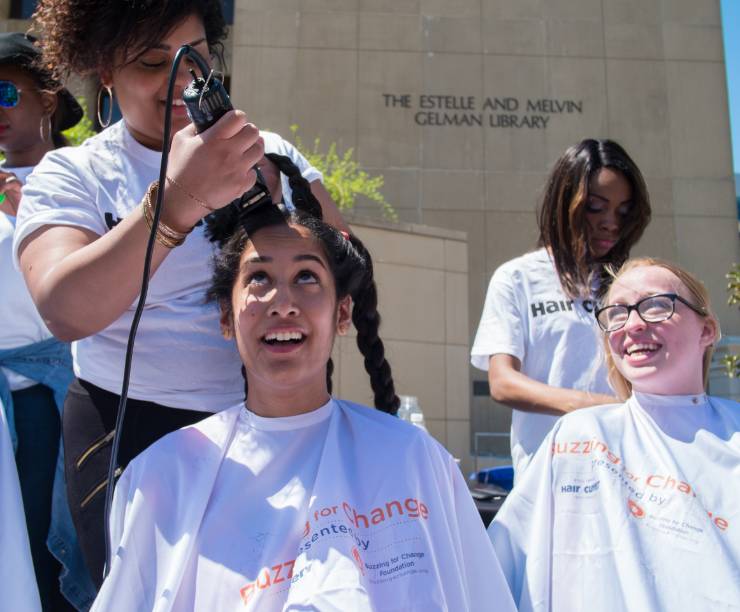 Two women smile as they get their heads shaved.