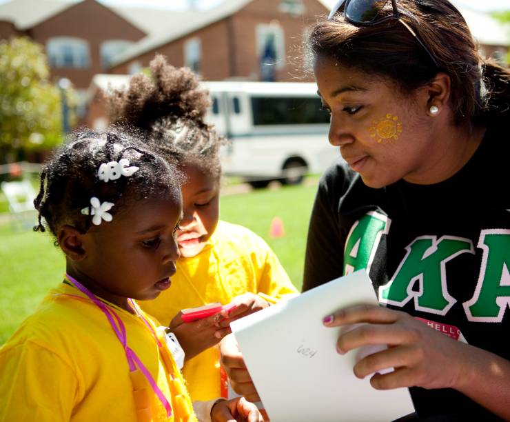 A student in a sorority shirt speaks with children.