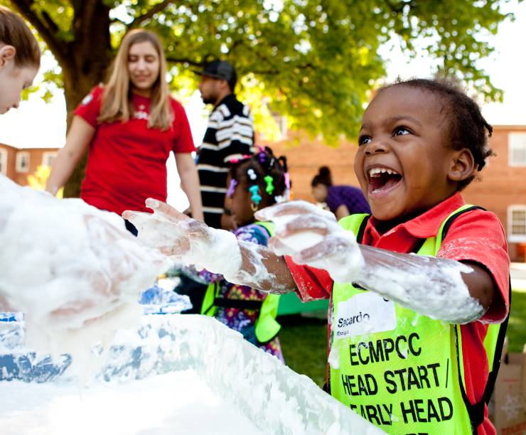 A young boy laughs and plays in foam with volunteers.