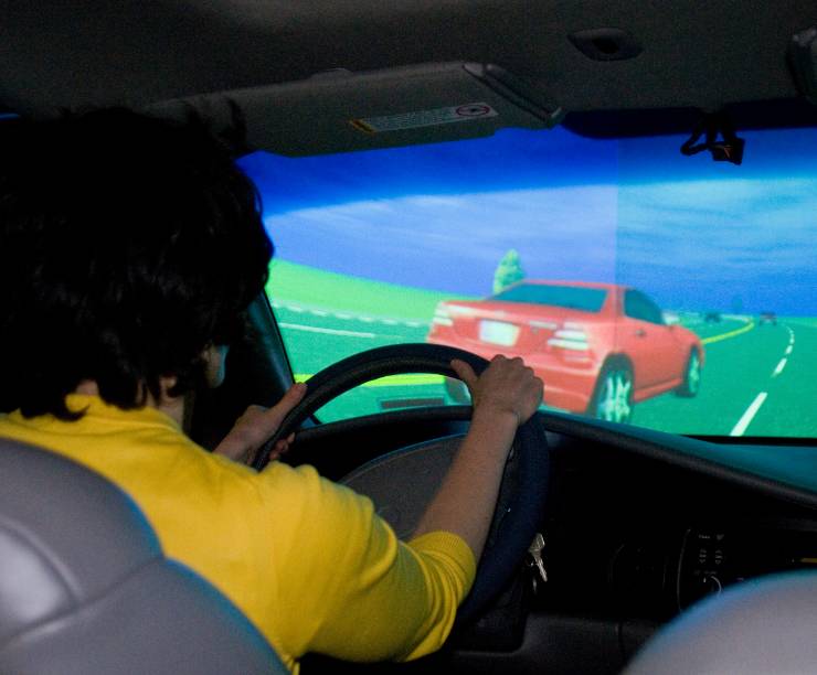 A driver in a test car looks at a simulation screen with a road scene.