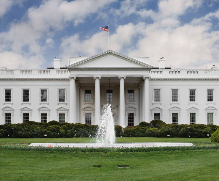 Exterior shot of the white house showing columns, a fountain and green grass.