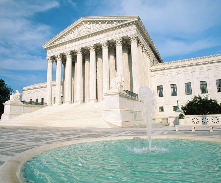 Exterior shot of Supreme Court showing white building with columns and a fountain in the foreground