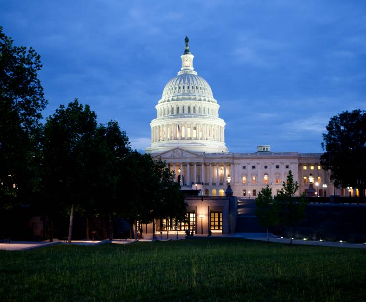 Exterior photo of capitol dome at dusk with blue sky and silhouetted trees.