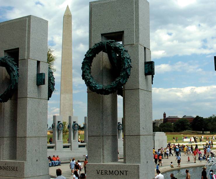 Rectangular columns with wreaths against a blue sky with the Washinton Monument in the background.