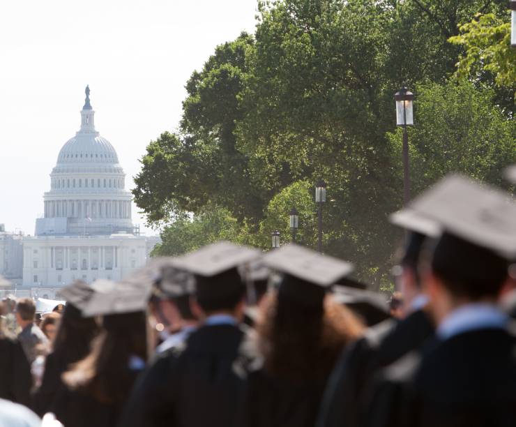 Graduates in academic regalia face the Capitol building during Commencement.