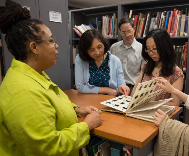 A group of people look at a book together in the library.