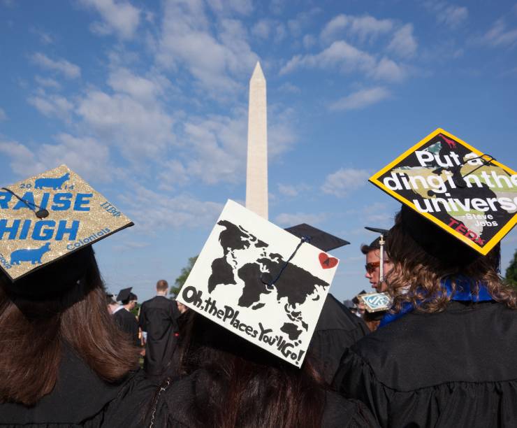 Graduates in academic regalia face the Washington Monument during Commencement.