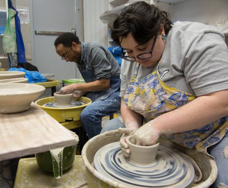 A man and woman create clay bowls at pottery wheels.