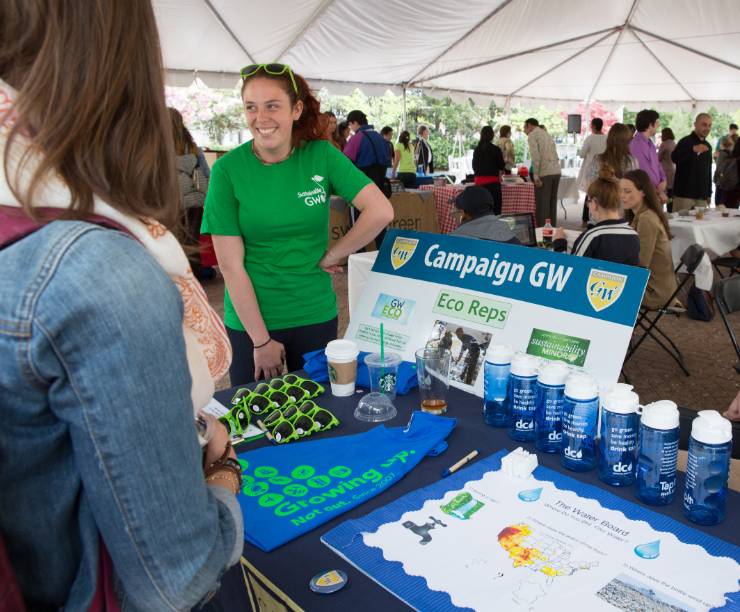 A man and woman talk to students at an Earth Day fair table.