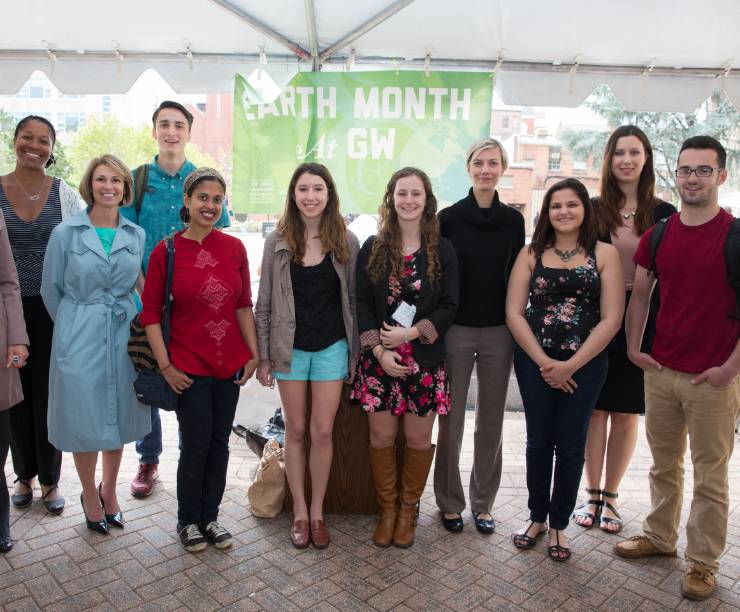 A group of students stand outside in front of an Earth Month banner.