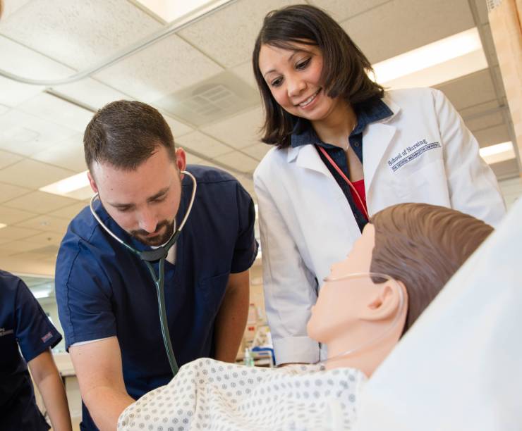 A student examines a simulation mannequin with a stethoscope as two other students and a professor observe.