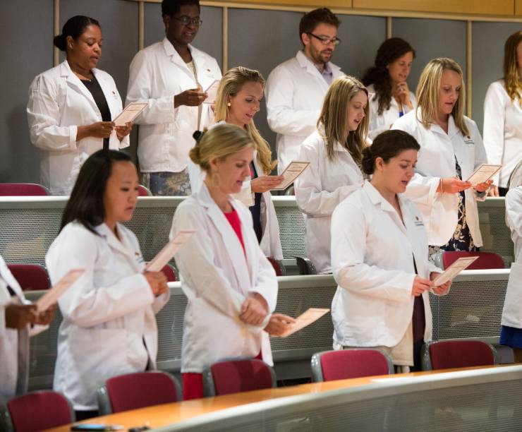 Nursing students in white coats reciting a ceremonial oath.