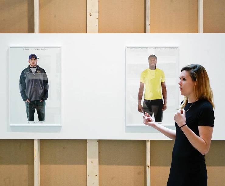 A woman speaks in front of two photographs on the wall.