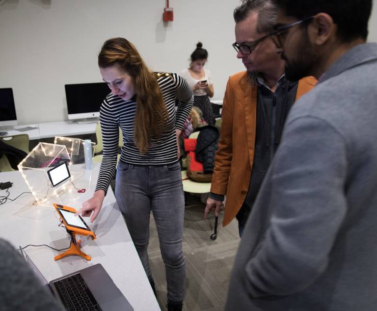 Two students and a professor look on as a student touches a screen as part of an interactive exhibit.