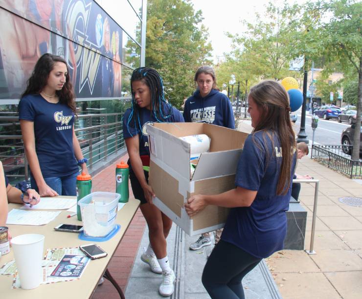 Members of the GW Lacrosse team are carrying a large box of donations collected for the Colonial Harvest annual food drive.