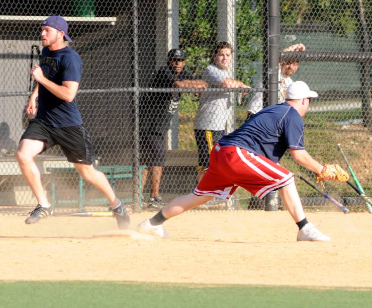 One man catches a ball as another runs toward a plate. Several other men watch in the background.