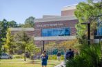 A female walking with her cell phone. A male with a backpack is walking towards Petway Hall.